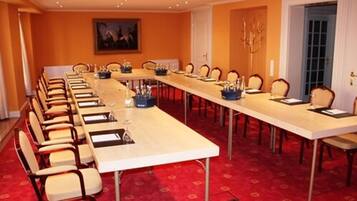 A conference room with a long table and chairs, red carpet, and a painting on the wall.