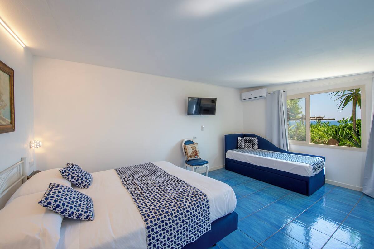 Habitación de hotel con dos camas, televisión, aire acondicionado y ventana con vista al mar.