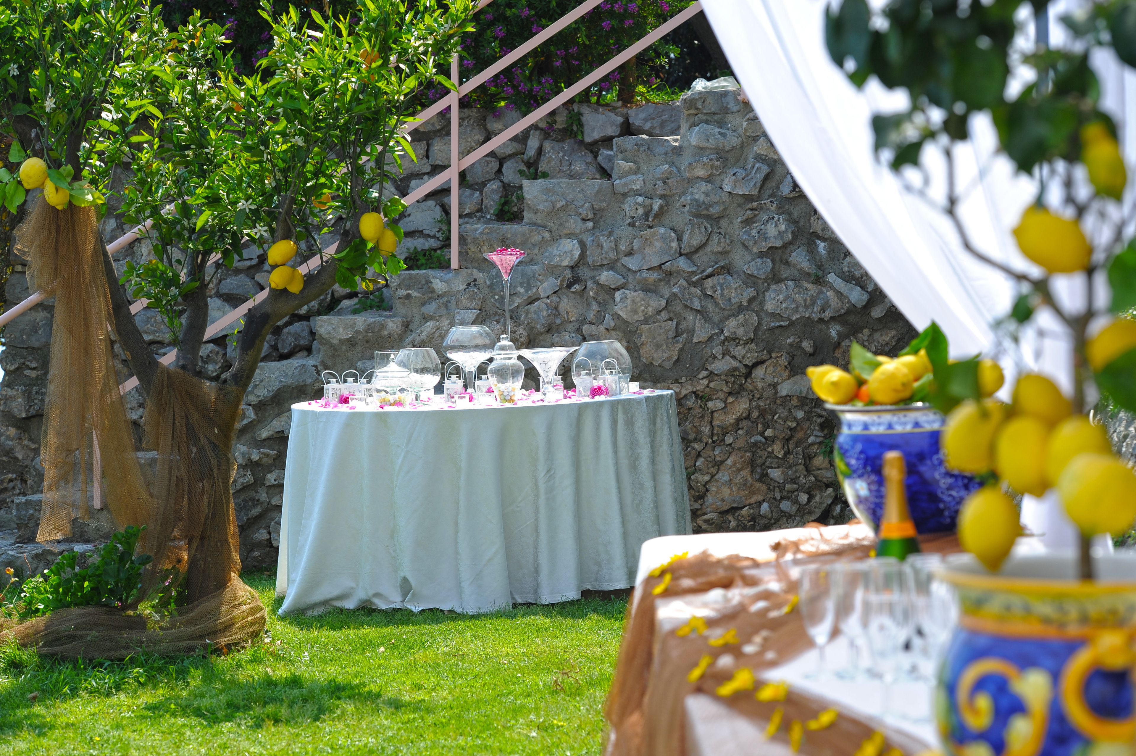 Un espacio de comedor al aire libre con una mesa lista para una comida, rodeado de follaje y un muro de piedra.