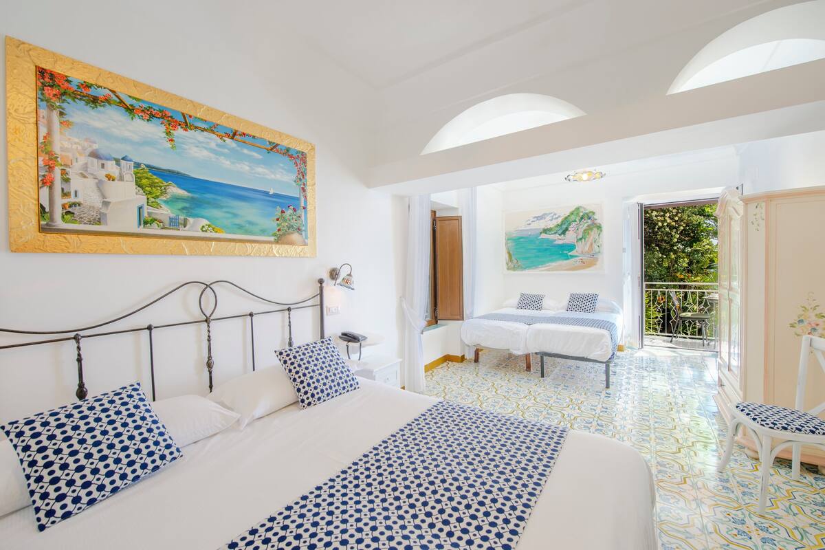Un dormitorio con una cama grande, un cuadro de una escena costera y un balcón con vistas al mar.