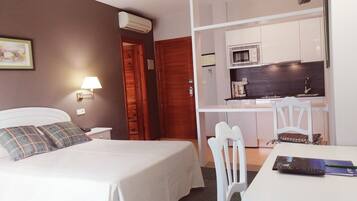 A bedroom with a bed, bedside table, lamp, and a small kitchenette with a microwave and coffee maker.