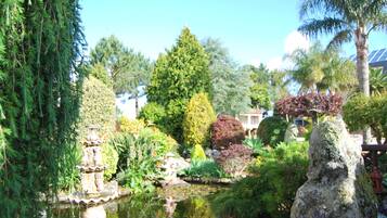Ein Garten mit Teich, einer Steinfigur und verschiedenen Bäumen.