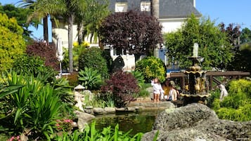 Un jardín con un estanque, una estatua y un edificio al fondo.