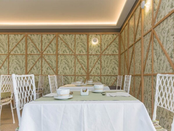 Comedor con una mesa dispuesta para cuatro personas, rodeada de sillas blancas, frente a un fondo de papel tapiz estampado.
