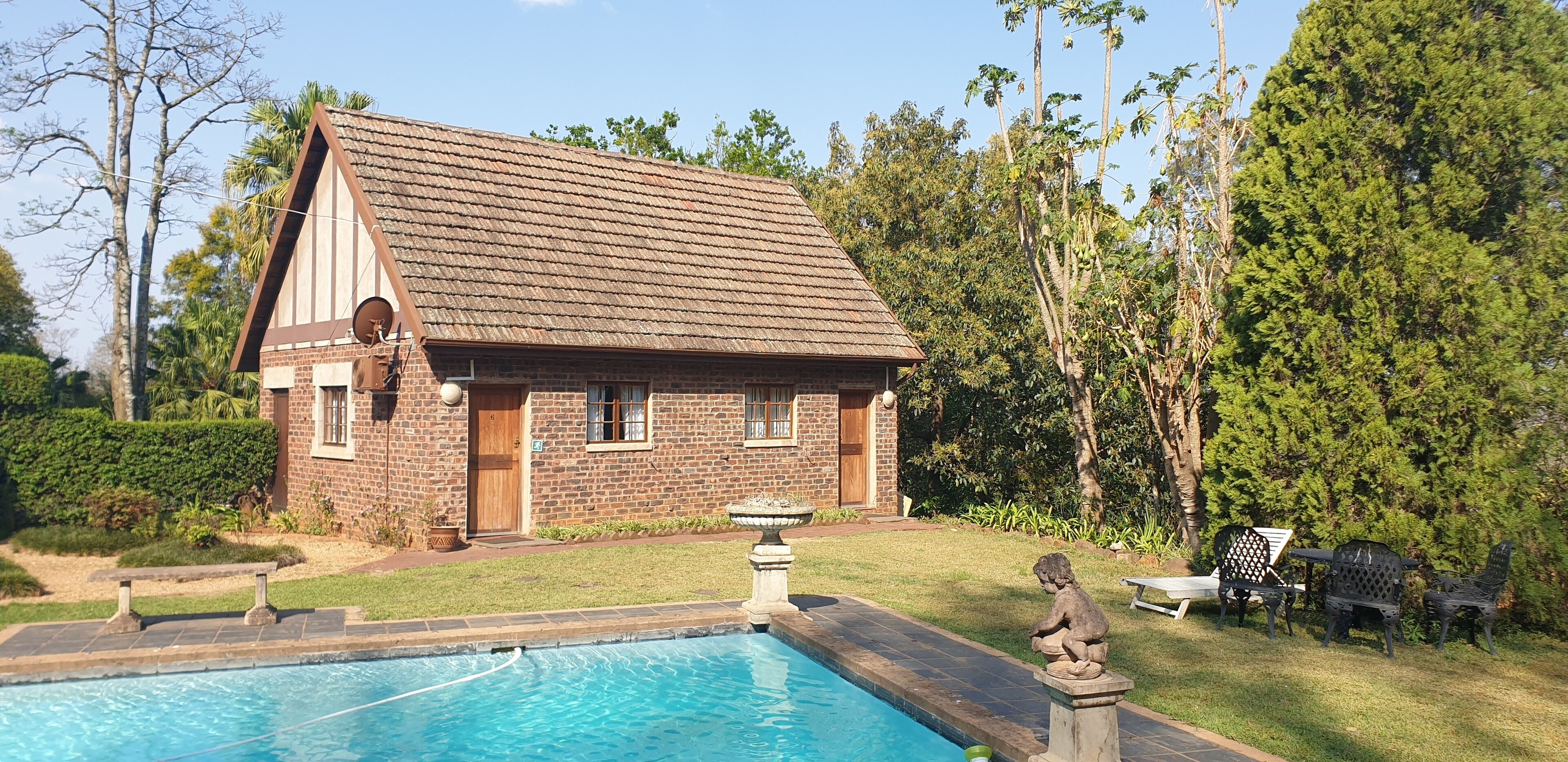 A brick house with a swimming pool, surrounded by greenery and trees.