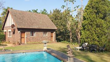 A brick house with a swimming pool, surrounded by greenery and trees.
