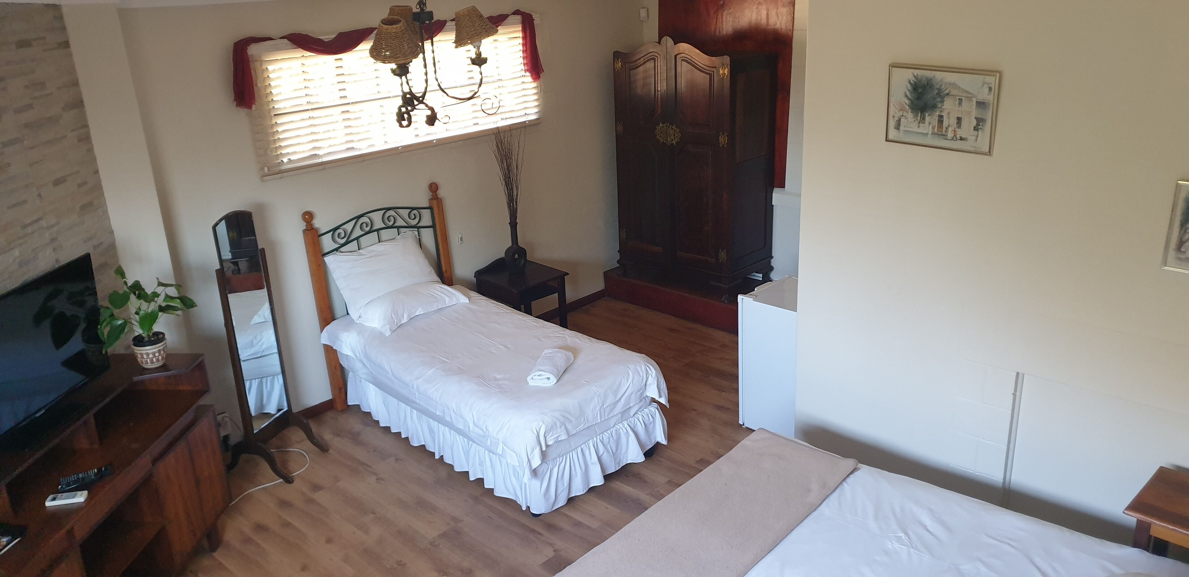 Un dormitorio con cama, mesita de noche, lámpara, armario y televisor sobre un soporte de madera.