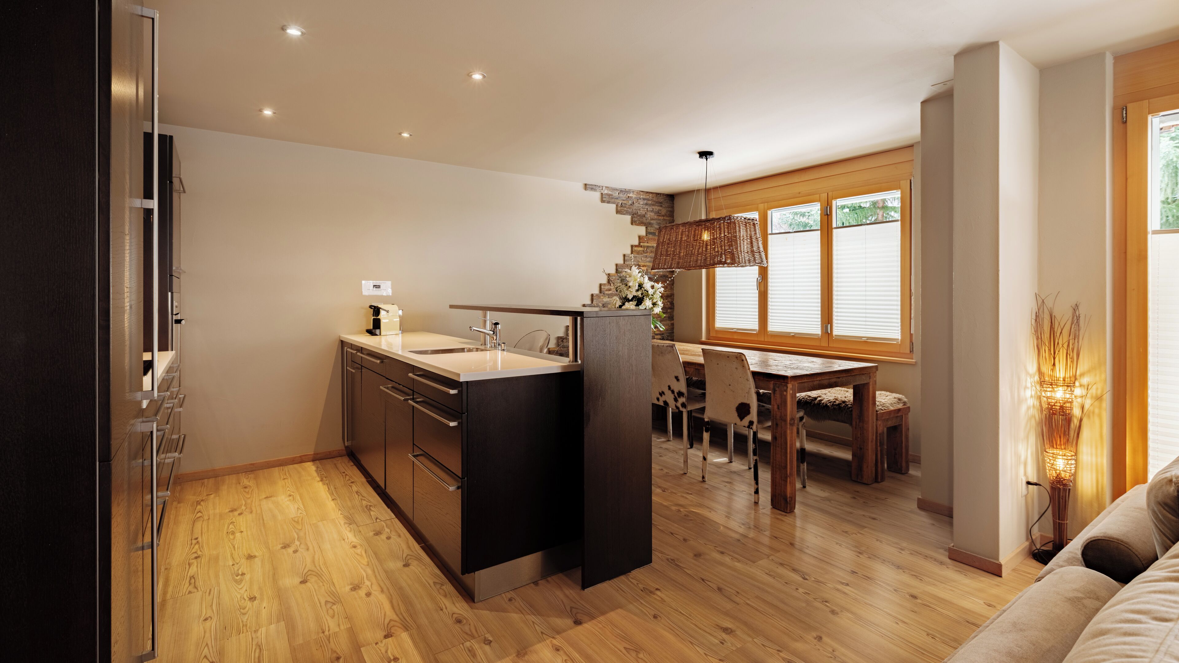 Una cocina moderna con una isla central, suelo de madera y un comedor con mesa y sillas de madera.