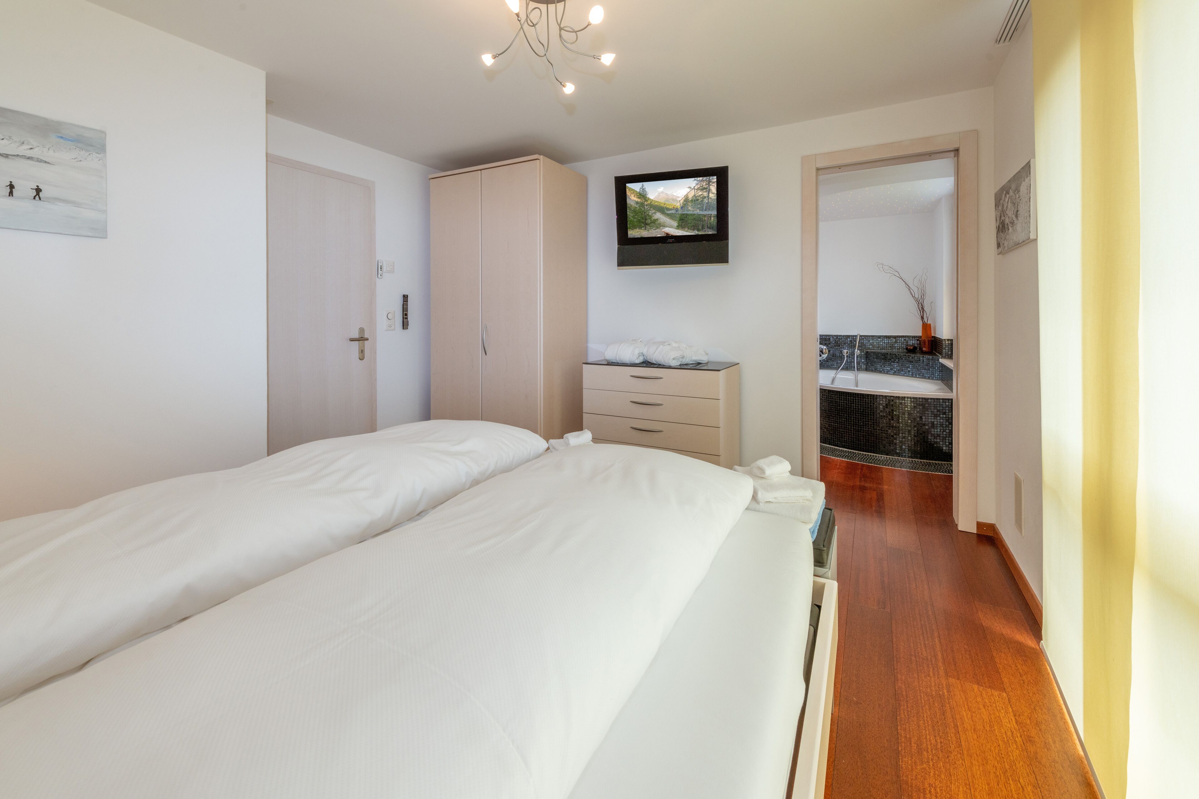 A bedroom with a large bed, a wardrobe, a television, and a bathroom visible through an open door.