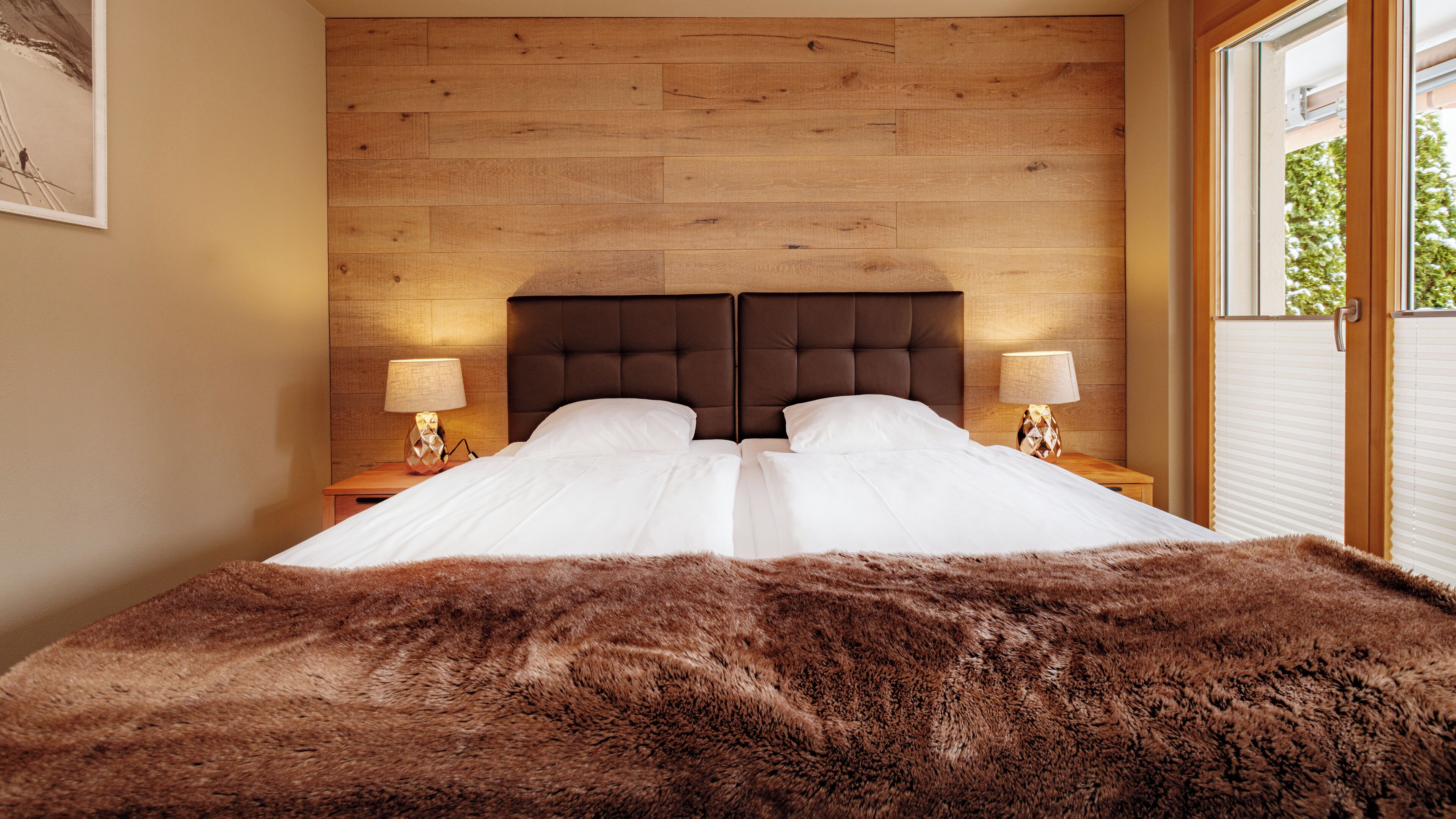 A double bed with a brown furry throw, wooden headboard, and two bedside lamps.
