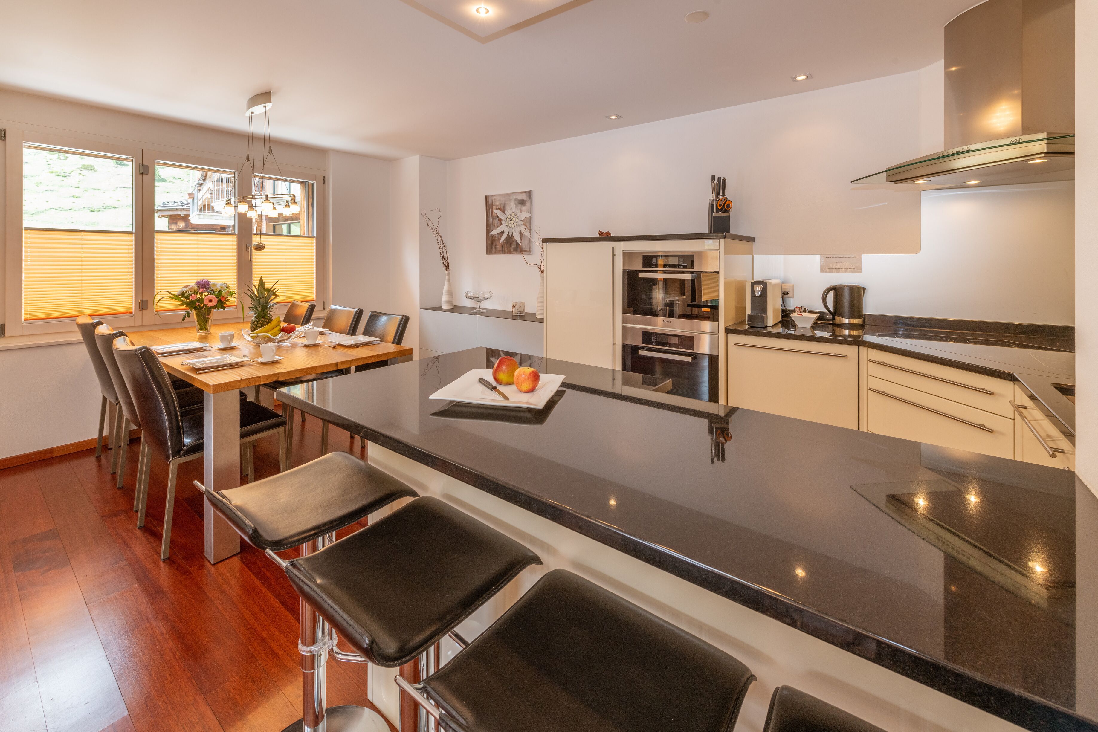 A modern kitchen with a central island, bar stools, and a dining area with chairs.