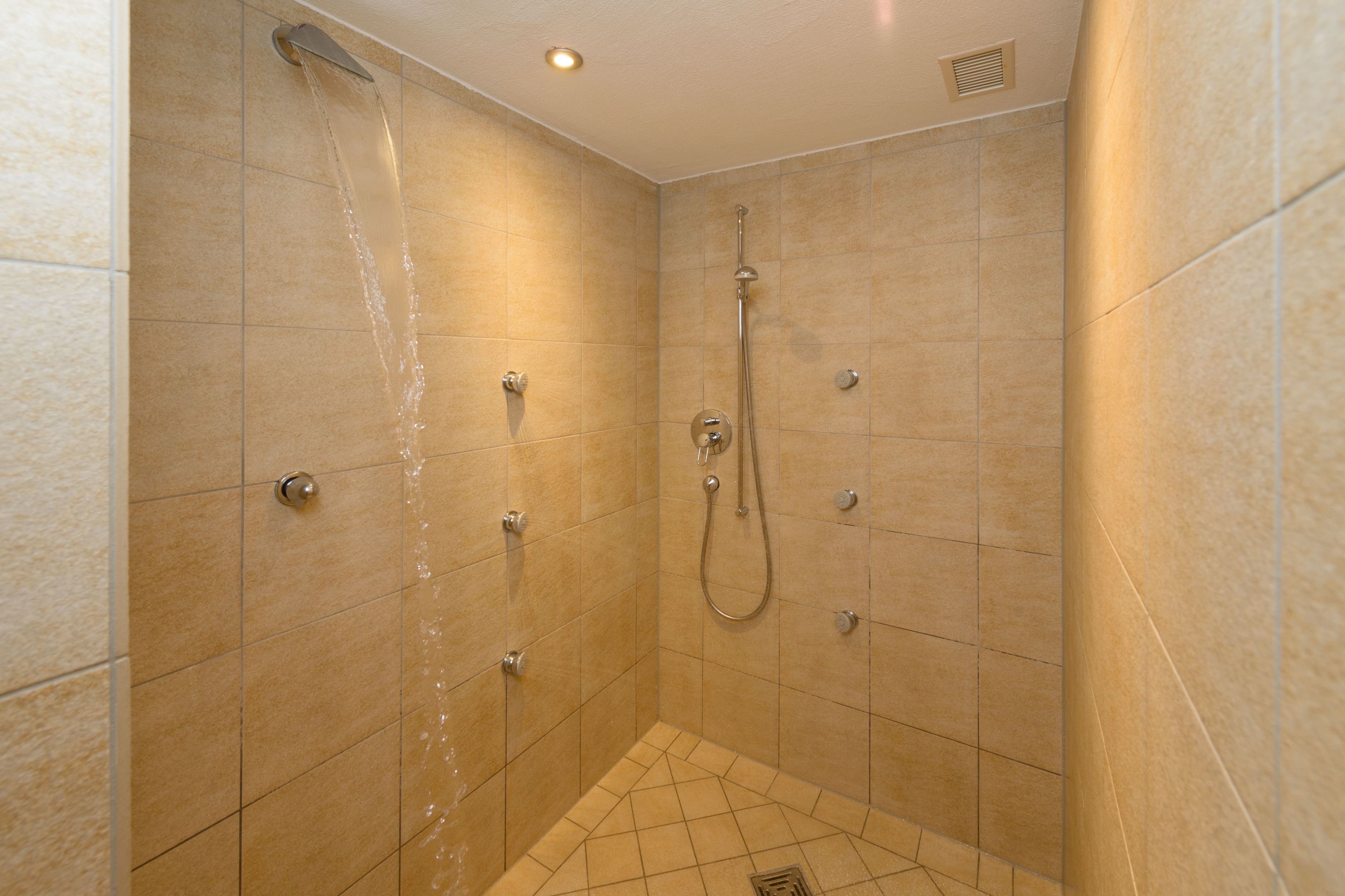 A small, tiled shower room with a handheld showerhead and a wall-mounted faucet.