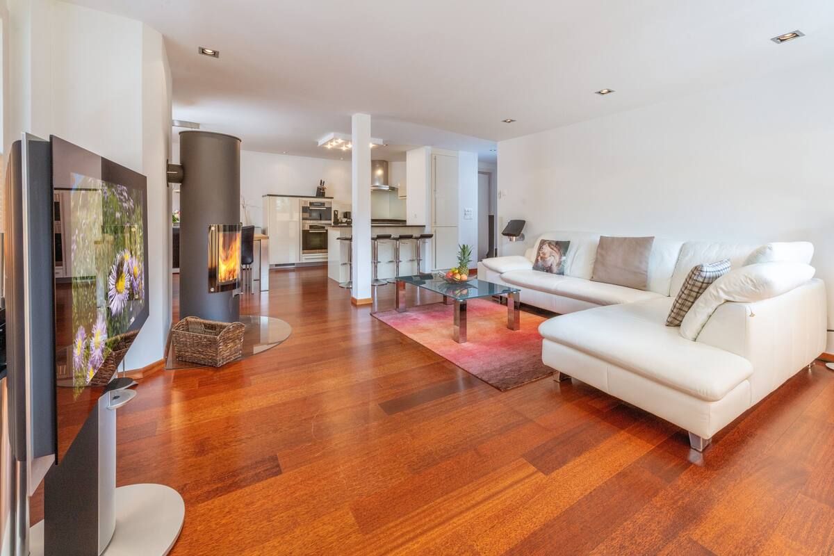 A modern living room with a white sofa, a flat-screen TV, and a fireplace.
