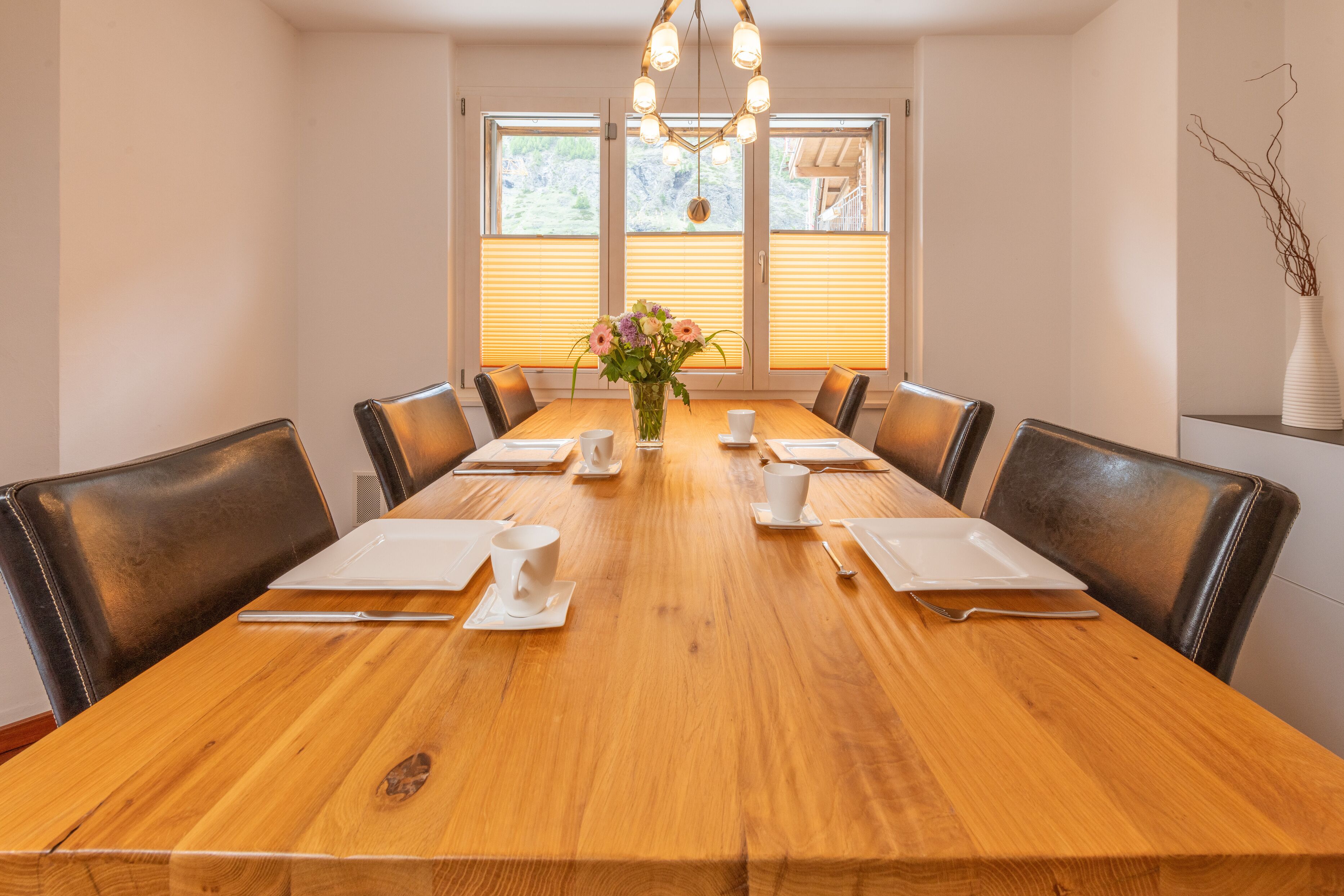 Un salón de conferencias con una mesa de madera, platos blancos, tazas y un jarrón de flores.