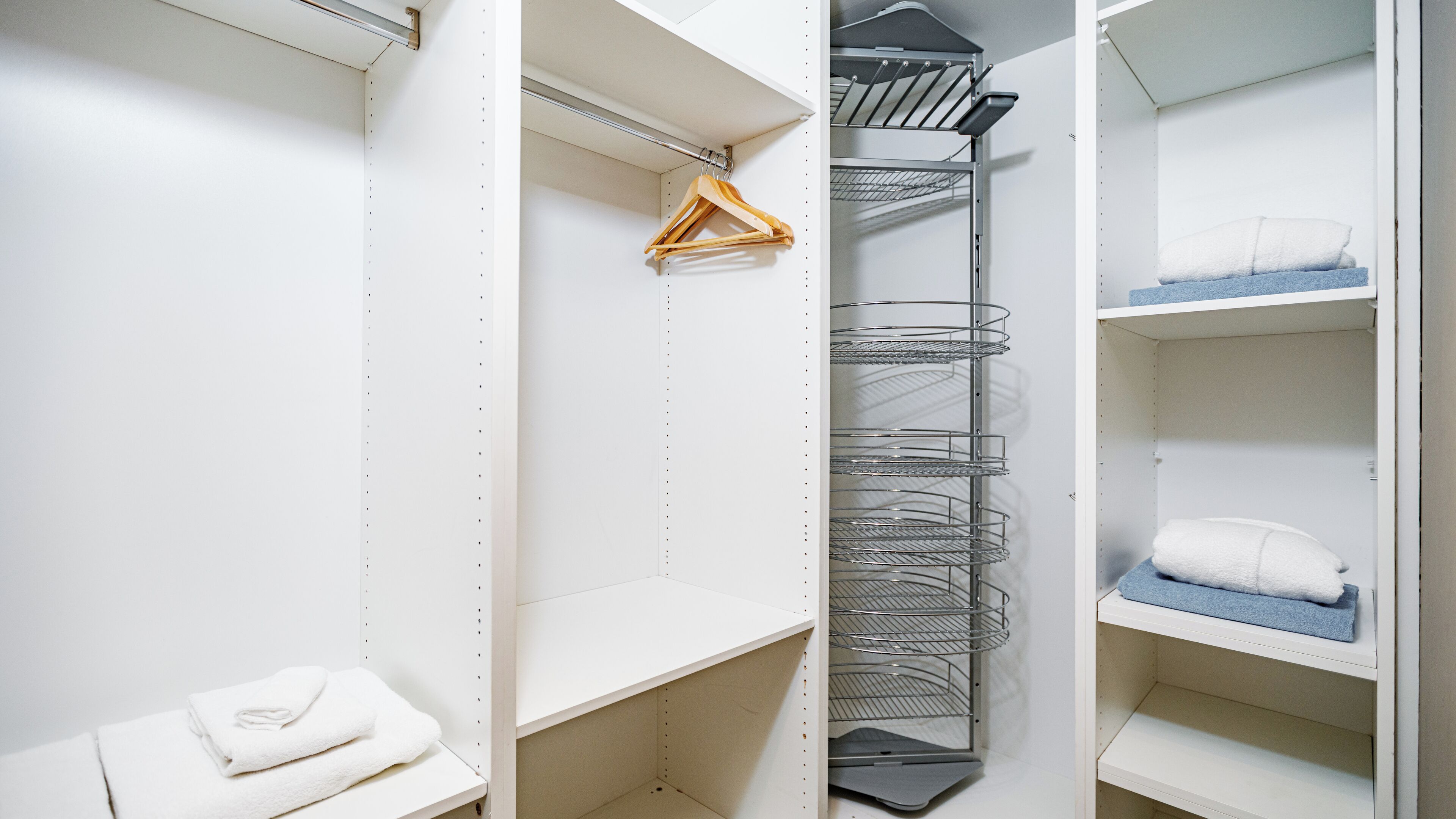 A walk-in closet with open shelves, a metal wire shelf unit, and a wooden hanger.