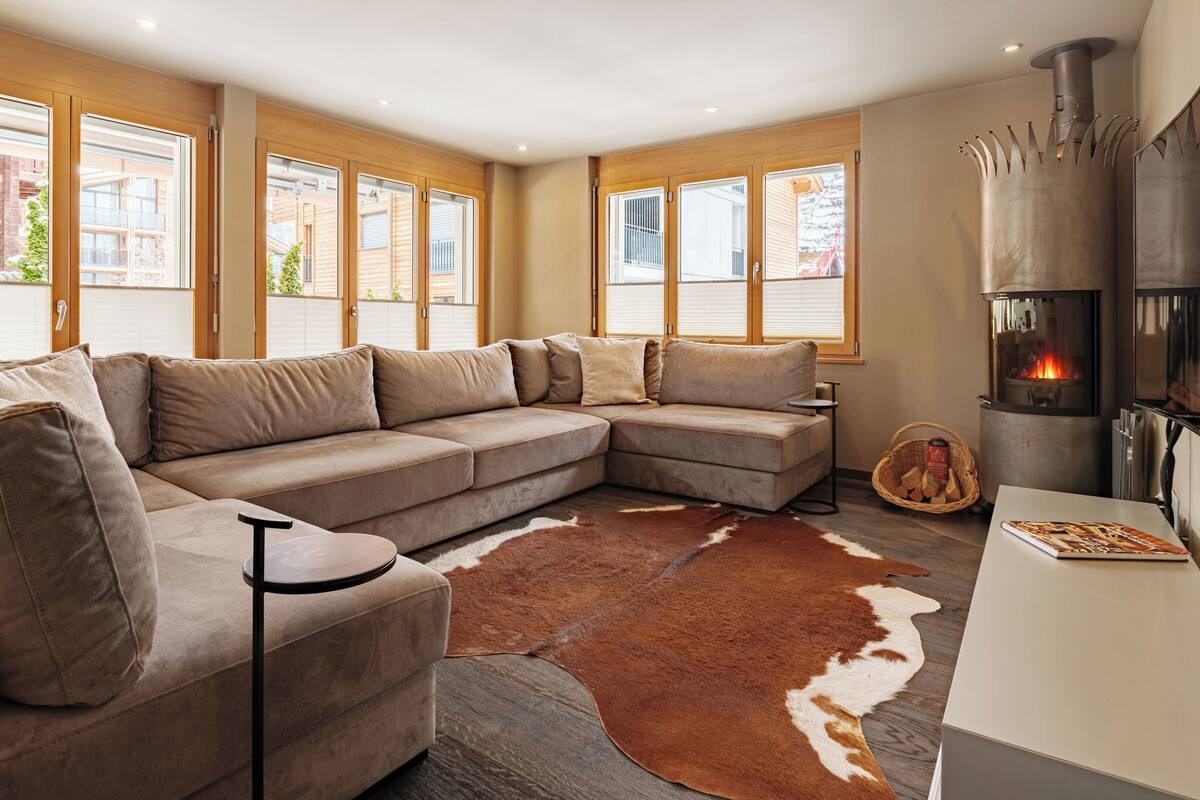 A modern living room with a sectional sofa, a fireplace, and large windows.