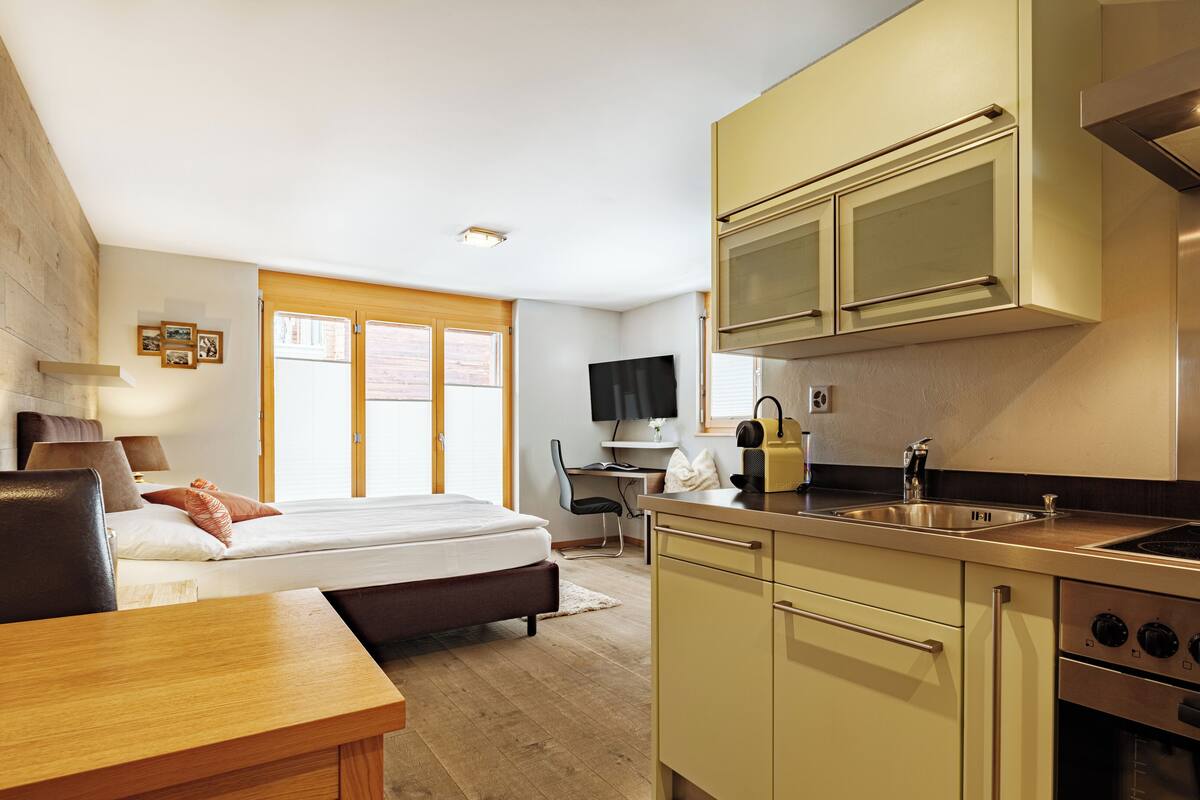 A compact hotel room with a bed, bedside table, and a kitchenette including a stove and sink.
