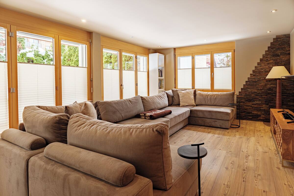 A modern living room with a sectional sofa, a small side table, and a staircase with a stone wall.
