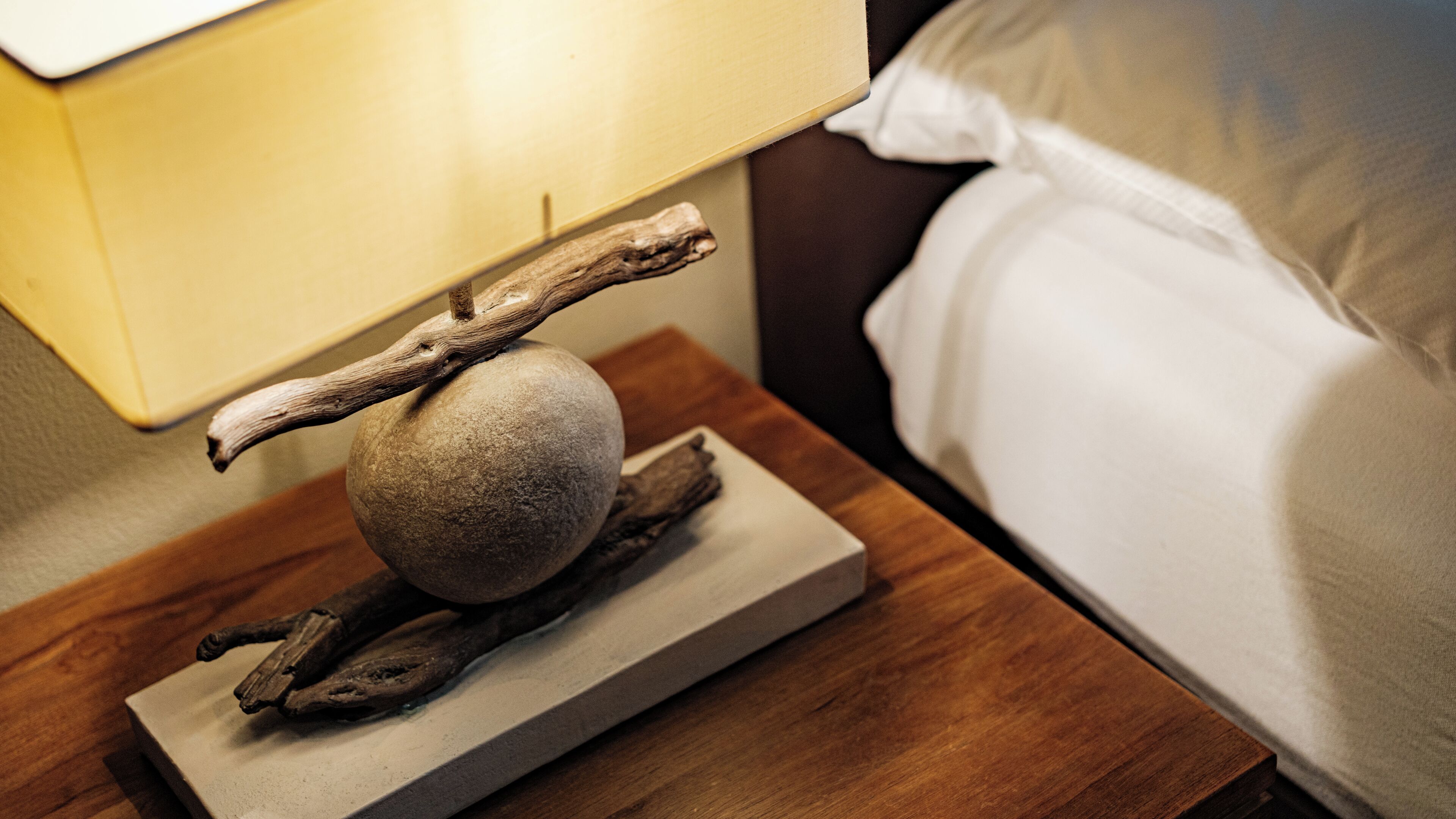 A bedside table with a lamp, a decorative stone, and a piece of driftwood.