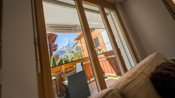 Una stanza con un'ampia porta-finestra scorrevole che dà su un balcone con vista su una montagna e un edificio in legno.