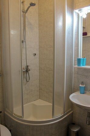 A shower with a glass door, a sink with a mirror, and a trash can. - Apartments Hrabar (Trogir)
