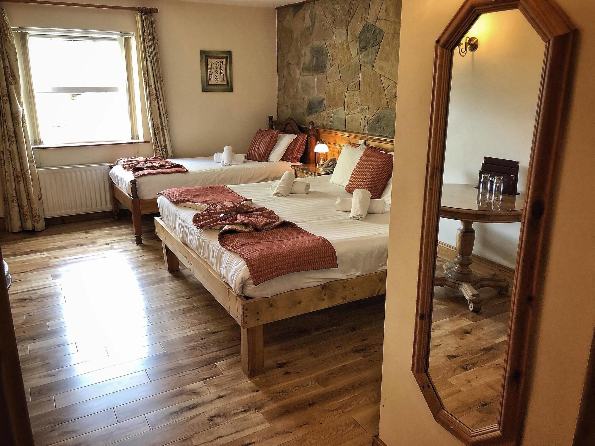 A hotel room with two wooden beds, a stone wall, a large mirror, and a window with curtains.