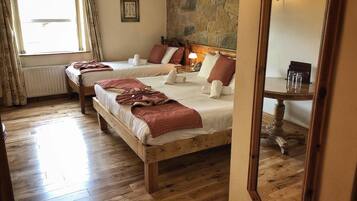 A hotel room with two wooden beds, a stone wall, a large mirror, and a window with curtains.