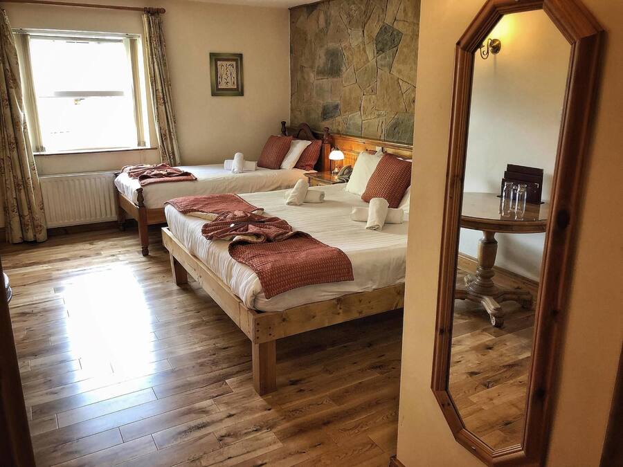 A hotel room with two wooden beds, a stone wall, a large mirror, and a window with curtains.
