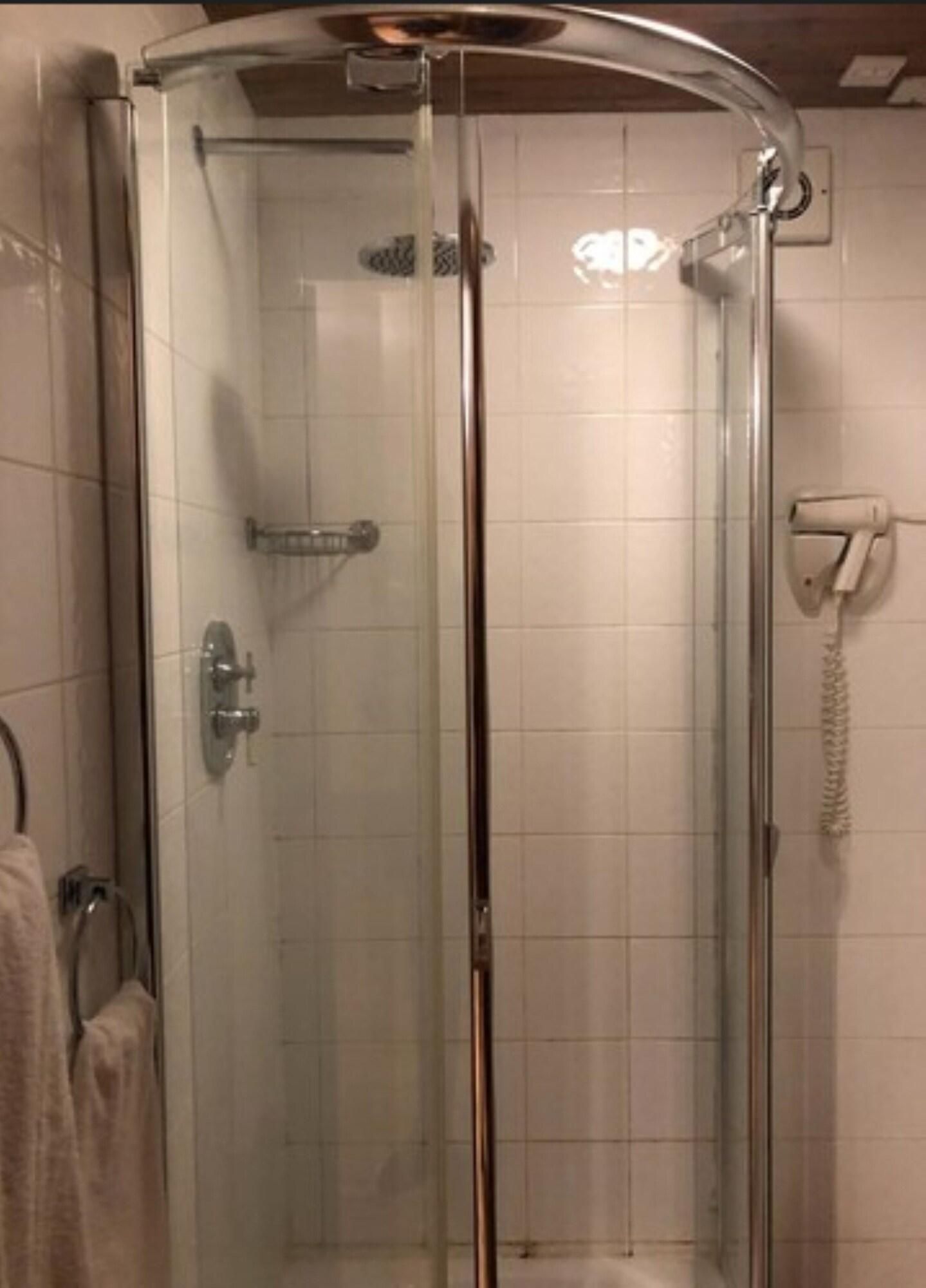 En brusekabine med glasvægge, håndbruser, håndklædeholder og telefon monteret på væggen.
