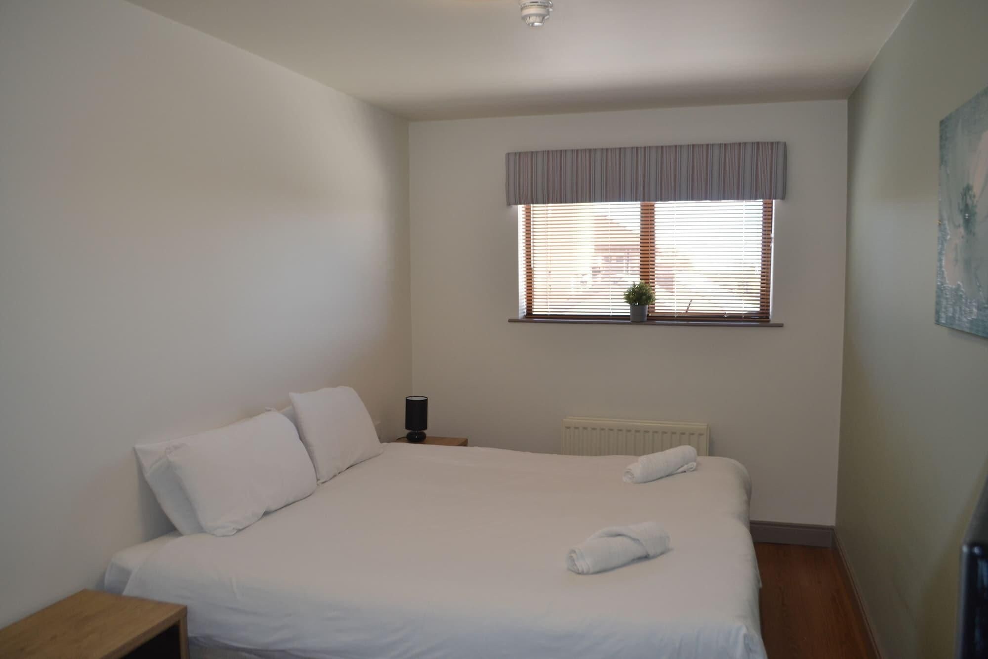 A bedroom with a bed, a radiator, a window with blinds, and a small table.