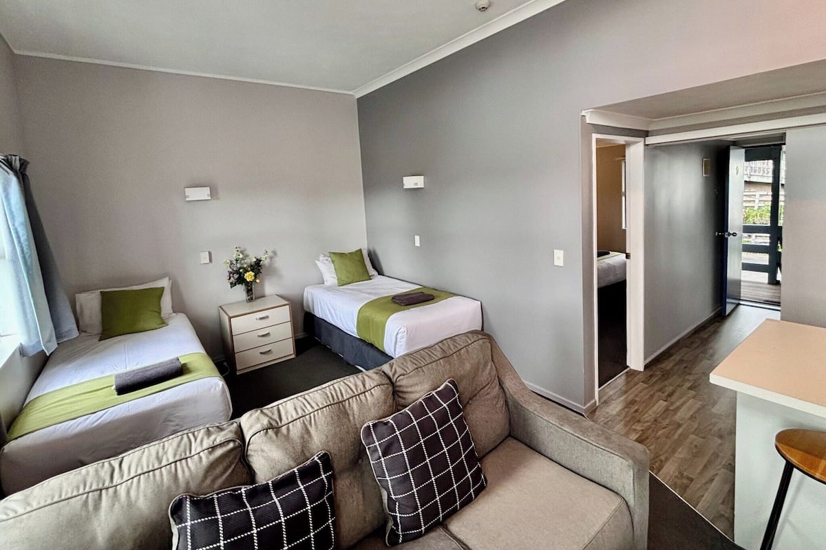 A hotel room with two beds, a sofa, a small table, and a kitchenette area.