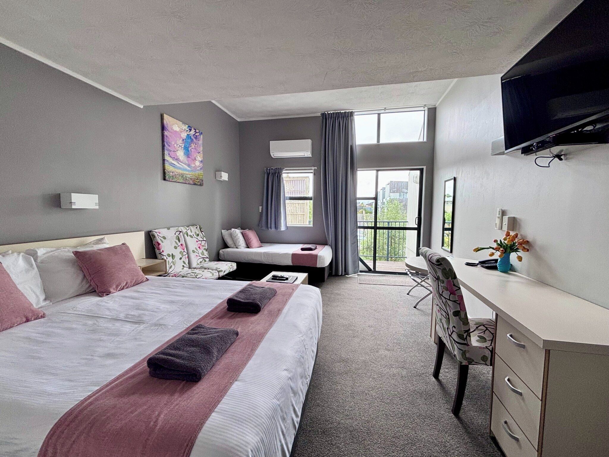 A hotel room with a large bed, a desk, a chair, and a TV.