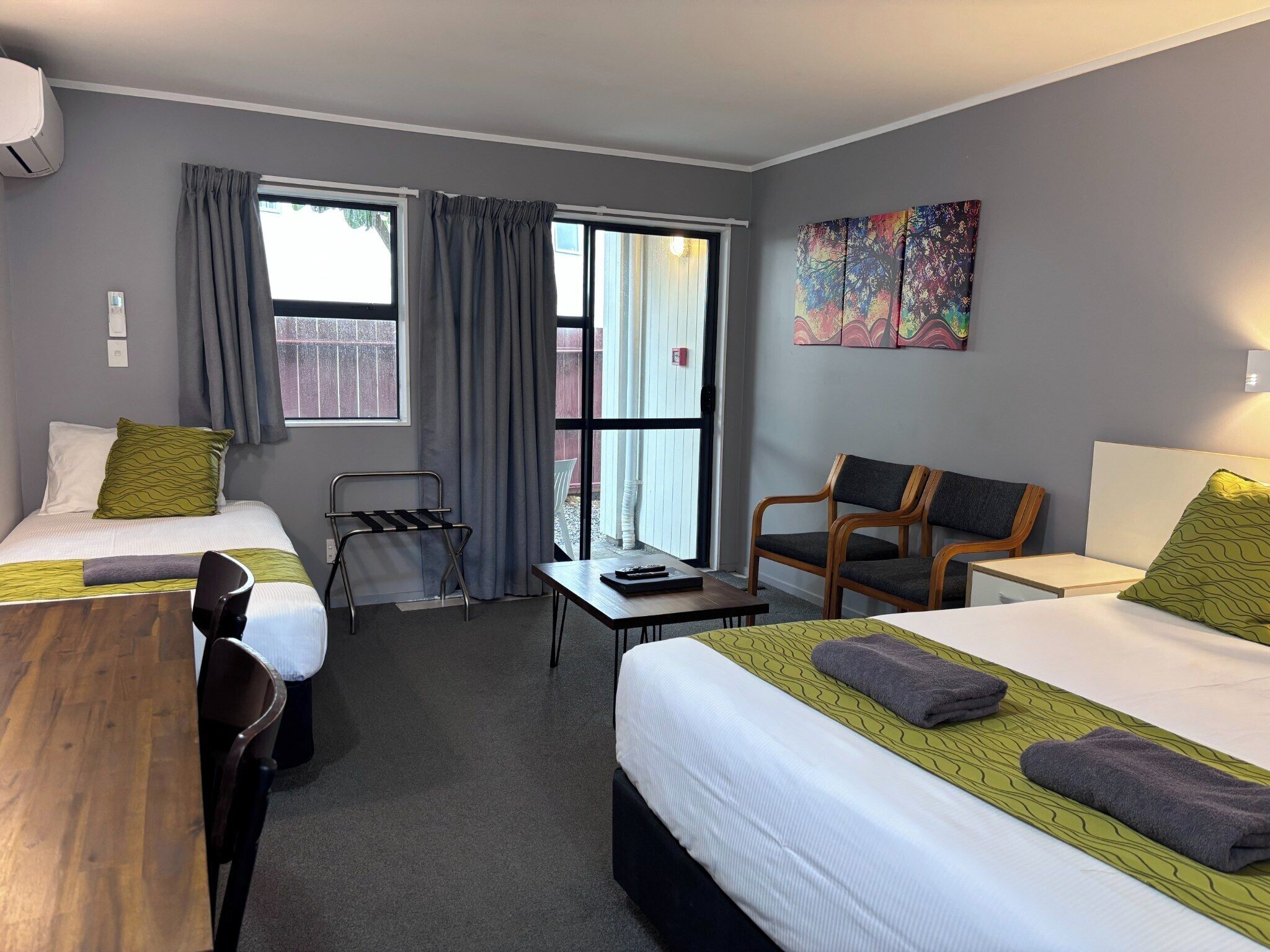 A hotel room with two beds, a desk, a chair, and a window with curtains.