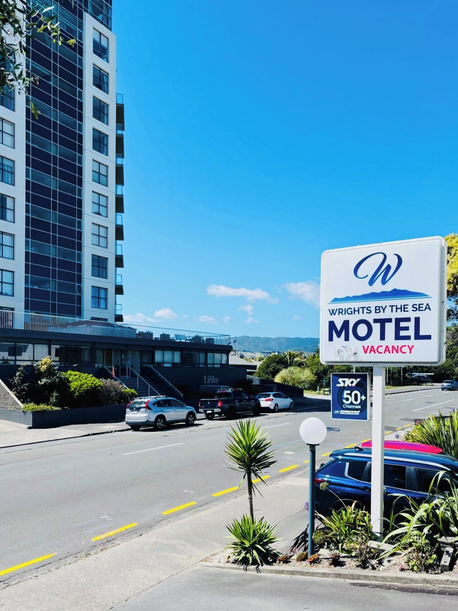 Placa de motel com um logotipo 'W', indicando 'Wrights by the Sea Motel', e uma placa 'Sky 50+', sugerindo serviço de TV via satélite.