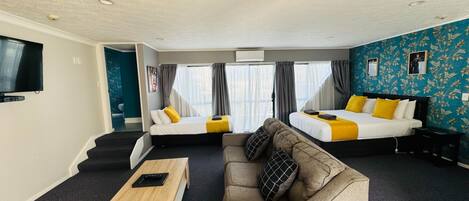 Habitación de hotel con dos camas, un sofá, una mesa de centro y un televisor.