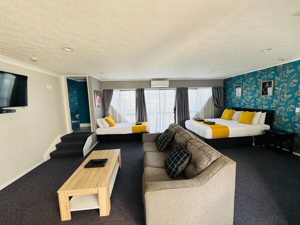 A hotel room with two beds, a sofa, a coffee table, and a TV. - Wrights By The Sea Motel (Paraparaumu)