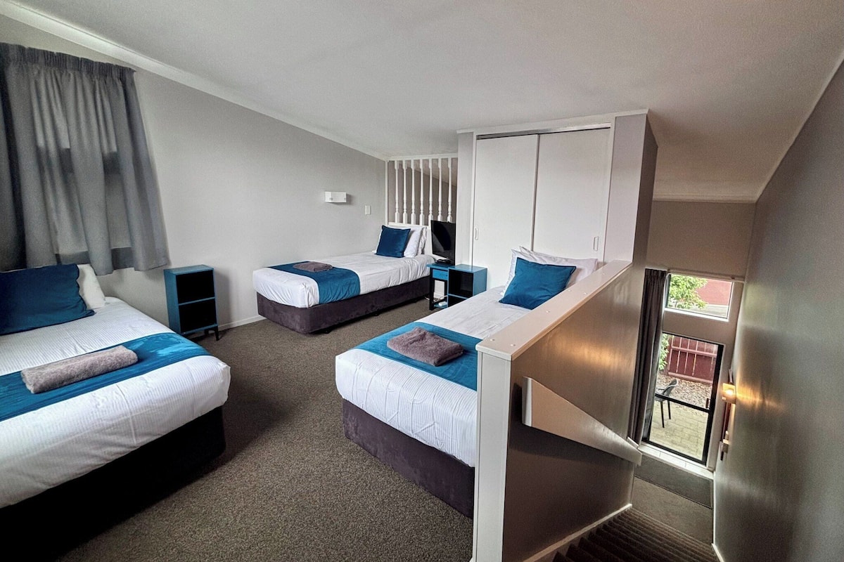 A hotel room with two beds, a desk, a TV, and a window with curtains.