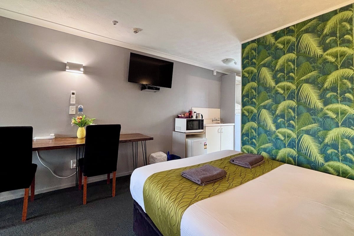 A hotel room with a bed, a desk with a chair, a television mounted on the wall, a microwave, and a small refrigerator.