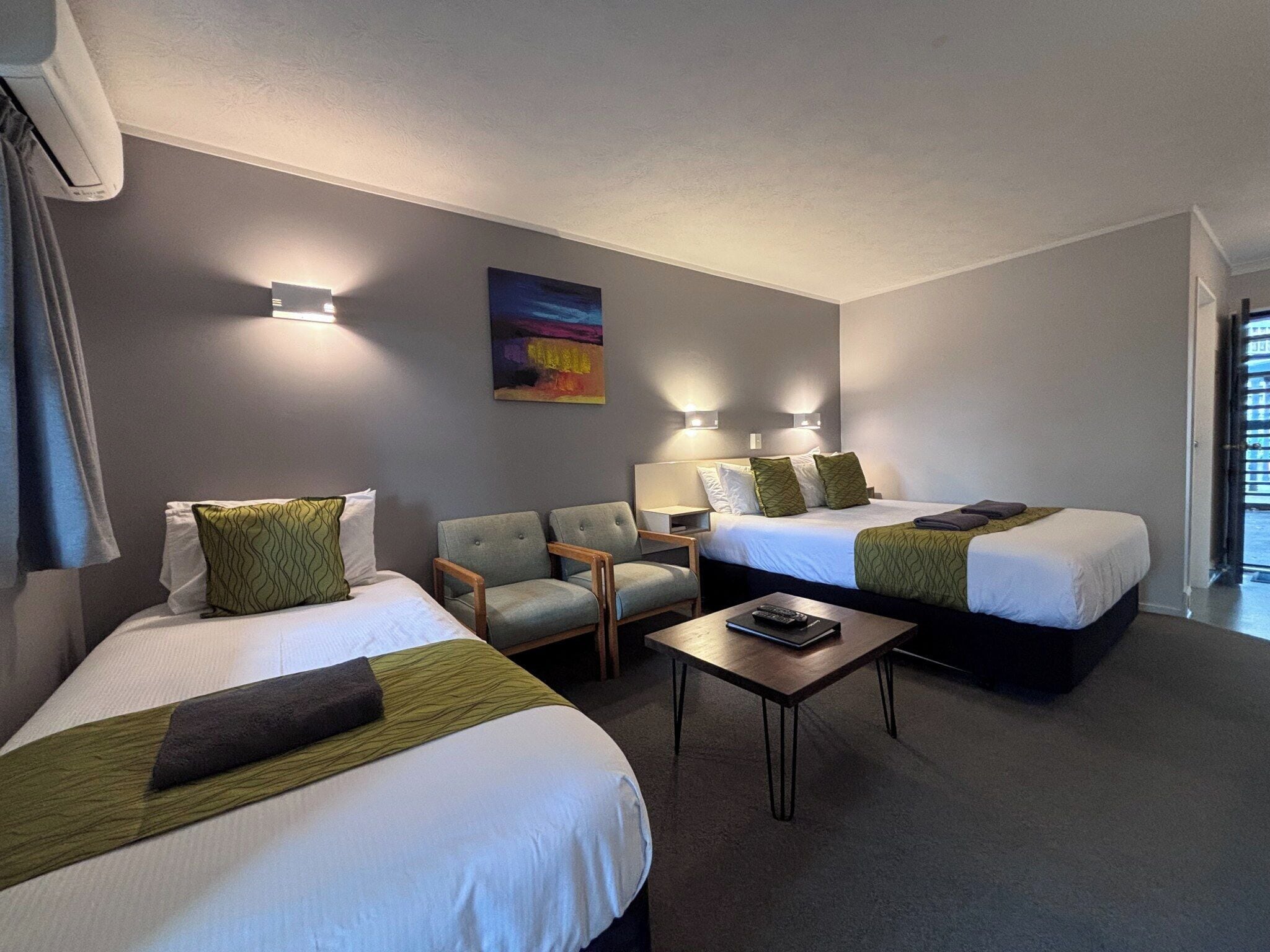 Habitación de hotel con dos camas, una silla, una mesita y un cuadro en la pared.