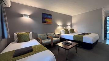 Habitación de hotel con dos camas, una silla, una mesita y un cuadro en la pared.