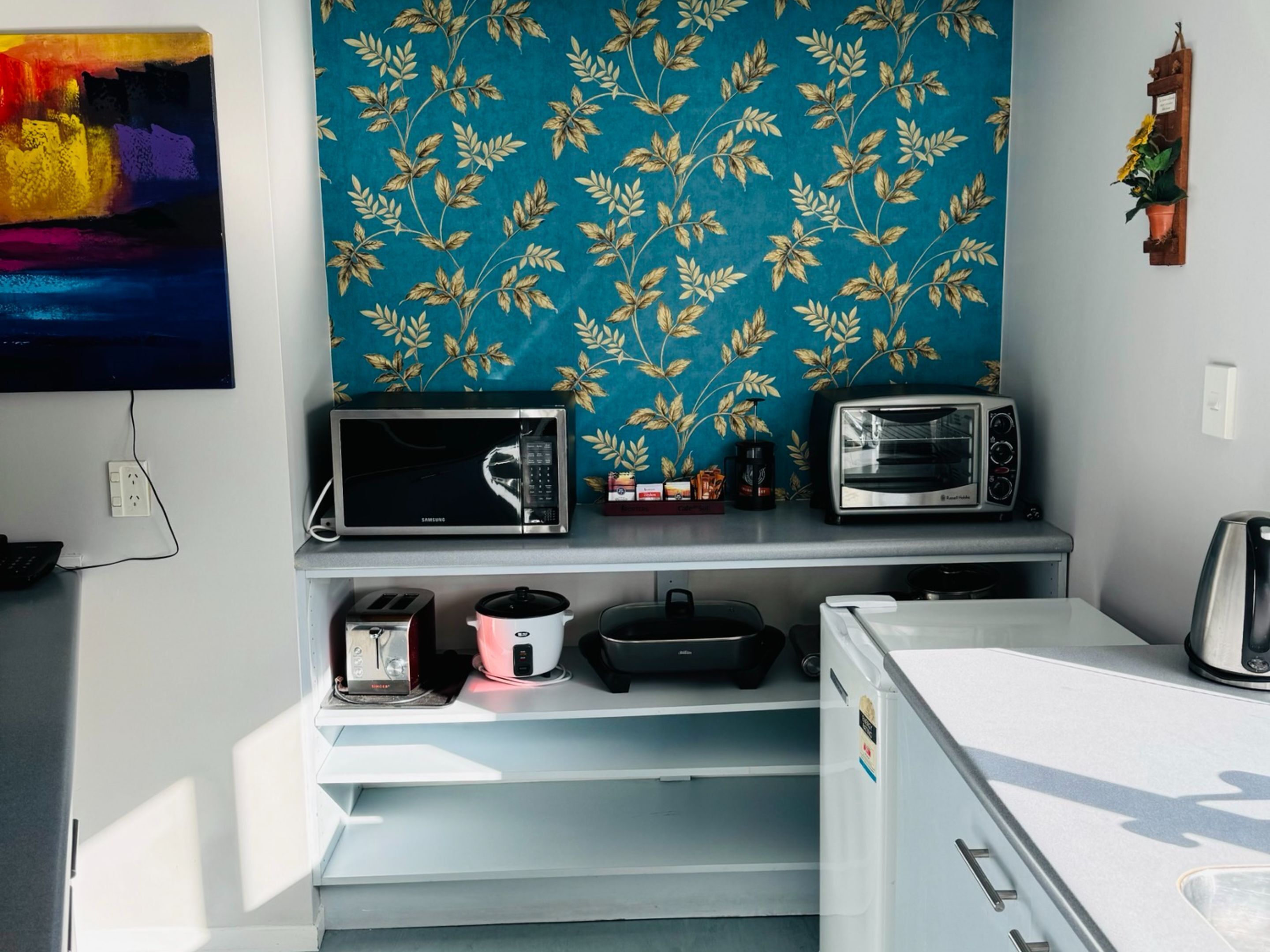 A compact kitchenette with a microwave, toaster, and coffee maker on a white countertop.