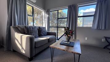 A modern living room with a grey sofa, a wooden coffee table, and large windows with grey curtains.