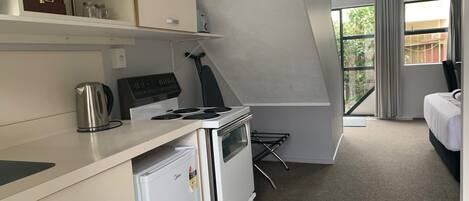 A compact kitchen with a stove, kettle, and refrigerator, a small dining area, and a bedroom with a window.