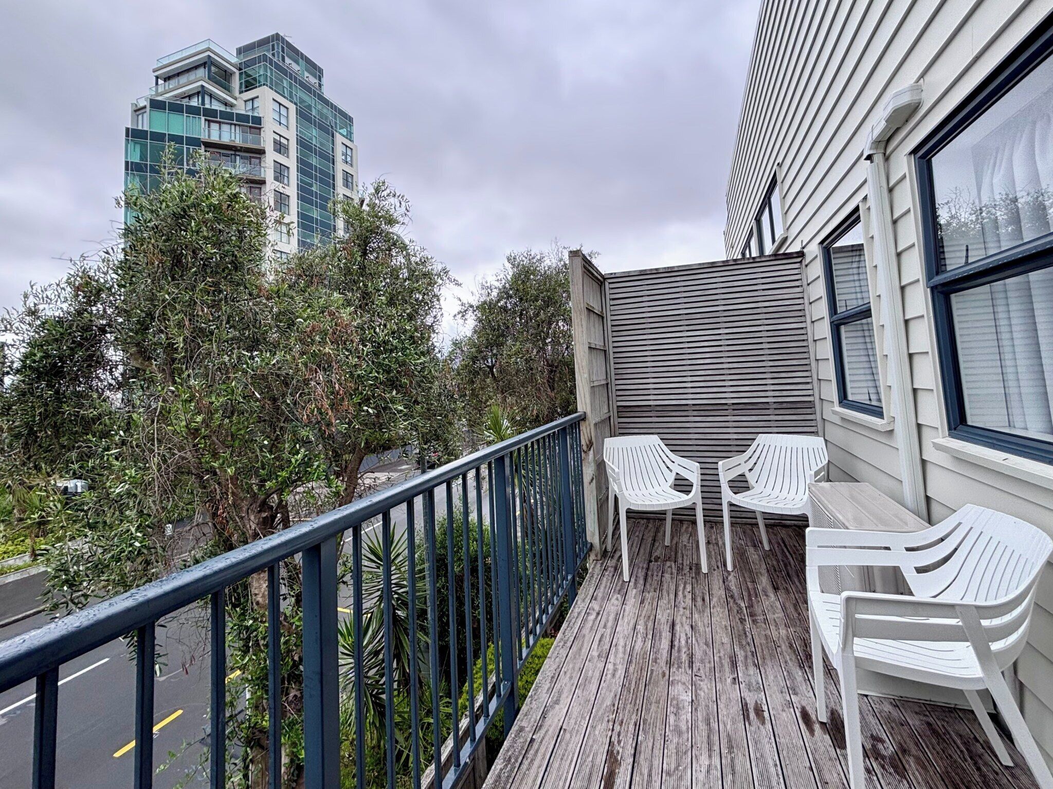 A balcony with a wooden floor, metal railing, and white plastic chairs.