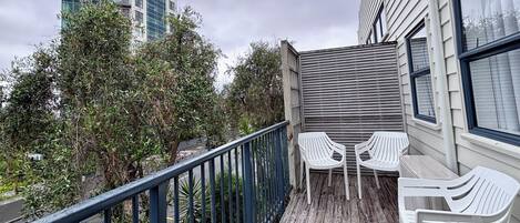 A balcony with a wooden floor, metal railing, and white plastic chairs.