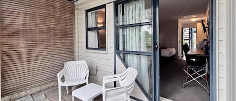 A room with a sliding glass door, a bed, a desk with a chair, and two white plastic chairs.