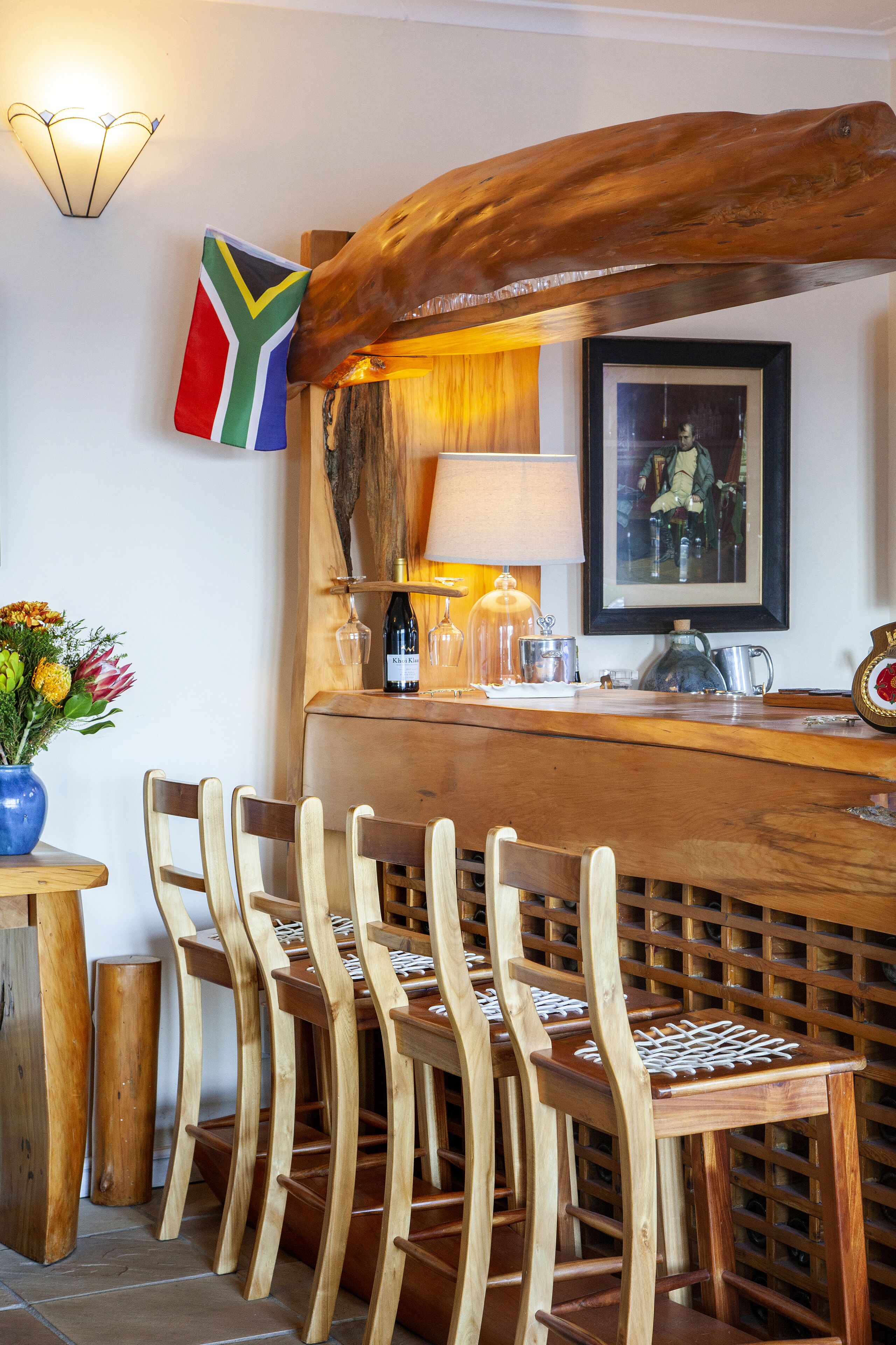 Uma área de bar com balcão de madeira, cadeiras, uma bandeira e um quadro na parede.