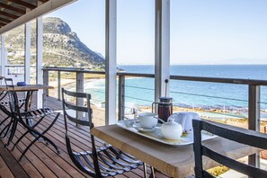 Eine Holzterrasse mit einem Tisch für zwei Personen, mit Blick auf Strand und Meer.