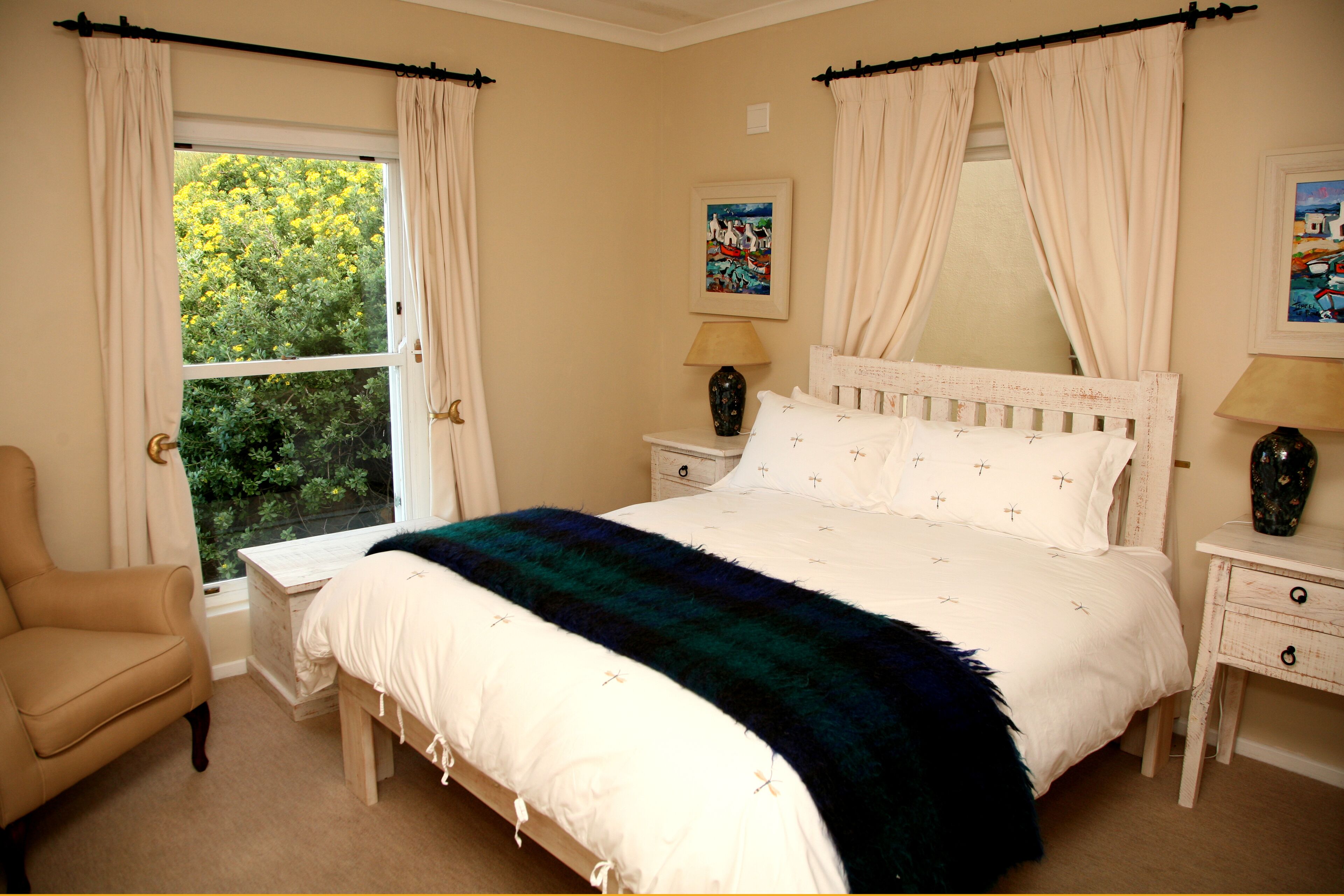 A bedroom with a bed, a chair, a nightstand, a lamp, and a window with curtains.