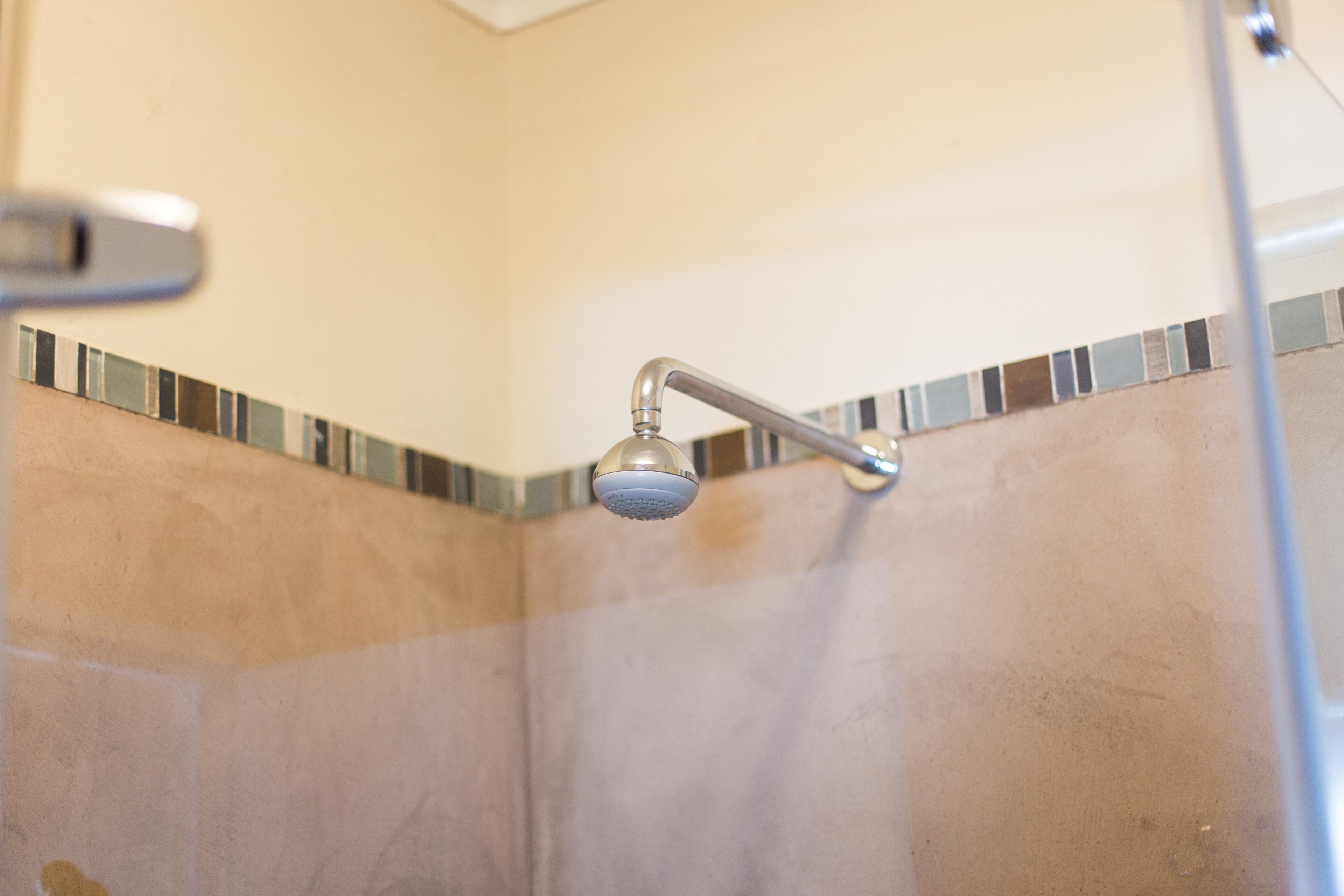 Una ducha con cabezal de ducha manual, diseño de azulejos en esquina y grifo metálico.